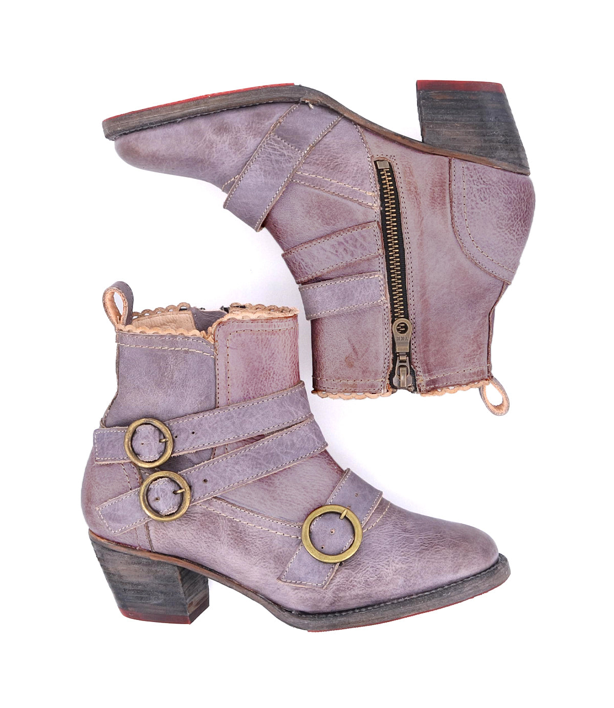 A pair of worn purple Bady ankle boots with side zippers, handmade leather, decorative brass buckles, and low heels by Oak Tree Farms.