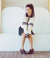 A girl sitting on a bench wearing a sweater and skirt, completing her neutral look with Oak Tree Farms lace-up front leather shoes named Janet.