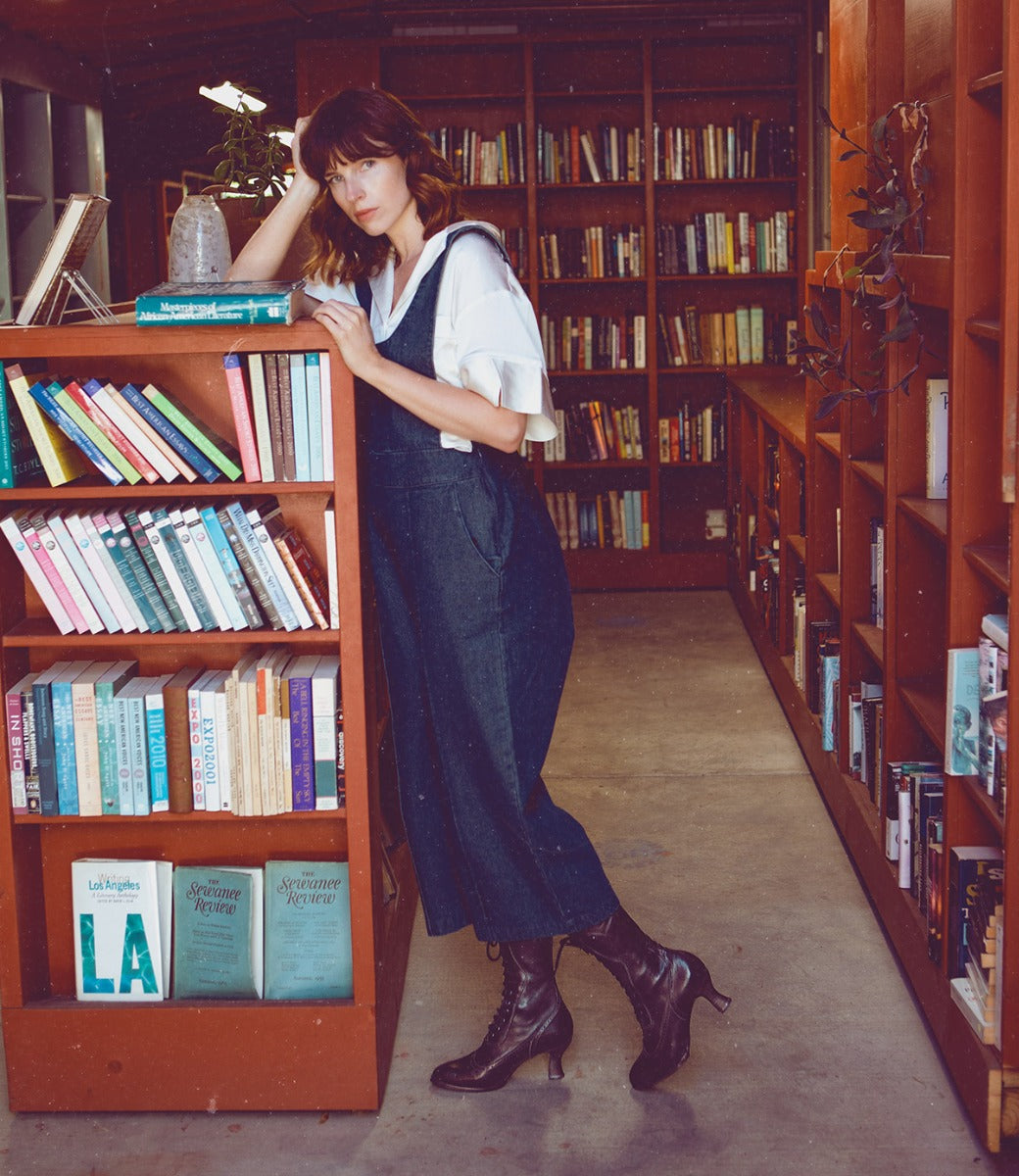 A woman with Oak Tree Farms Jasmine leather boots leaning against a bookcase in a library.