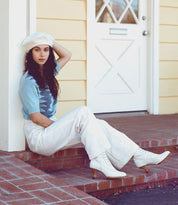 A woman, wearing Oak Tree Farms leather boots named Jasmine, is sitting on the steps of a house.