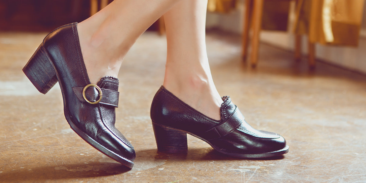 A woman's legs are standing on a wooden floor in black shoes.