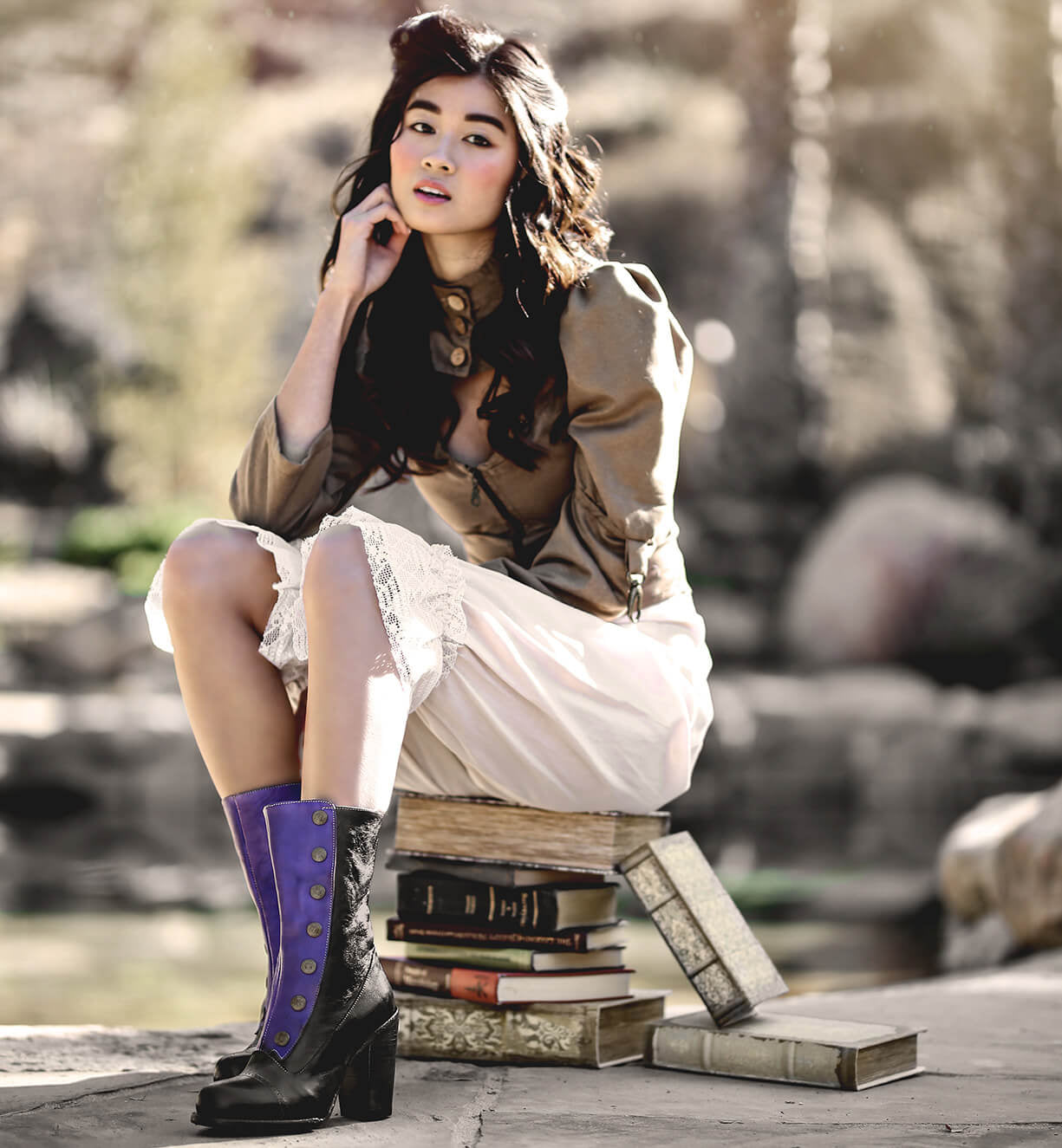 A woman sitting on a stack of books, wearing an Amelia two-tone color leather jacket by Oak Tree Farms.