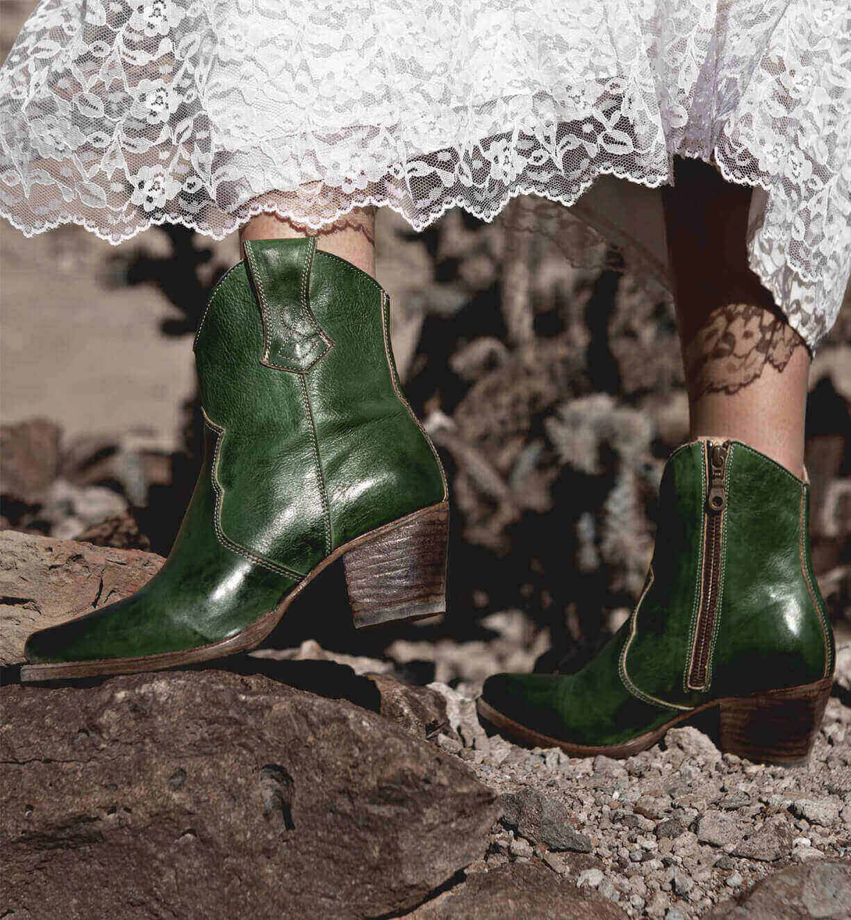 A woman in a white dress is standing on rocks in Oak Tree Farms Baila boots.