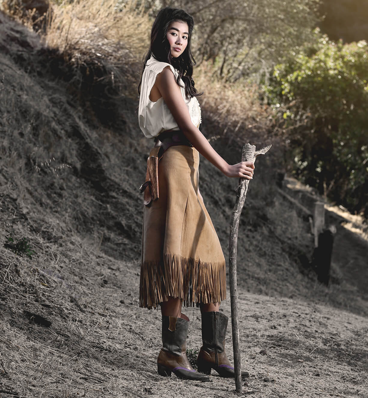 Oak Tree Farms, a woman in a cowboy outfit, holding a stick while donning leather boots.