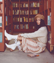 A woman seated on the floor in front of a bookshelf, wearing seductive black leather Oak Tree Farms Biddy boots.