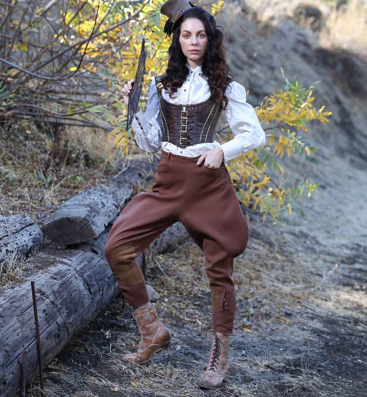 A woman in a Victorian style brown outfit, standing in a wooded area, holding an Eleanor gun of uncompromising quality made by Oak Tree Farms.