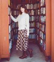 An uncompromising quality Eleanor woman in a plaid skirt standing in front of a bookshelf. (Brand Name: Oak Tree Farms)