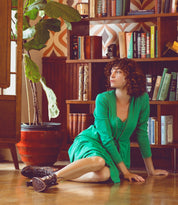 A woman in a green dress, Jacquelyn by Oak Tree Farms, handcrafted, sitting on the floor.