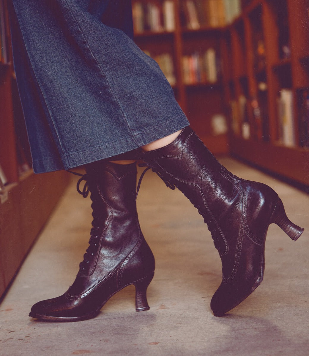 A woman wearing a pair of Oak Tree Farms Jasmine leather boots in a library.
