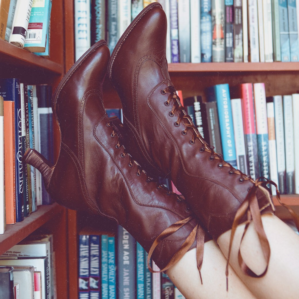 A woman wearing the Oak Tree Farms Jasmine hand dyed Black Rustic leather boots in front of a bookshelf.