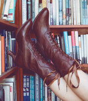 A woman wearing the Oak Tree Farms Jasmine hand dyed Black Rustic leather boots in front of a bookshelf.