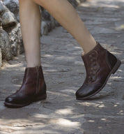 A woman wearing brown leather Josephine boots from Oak Tree Farms with a YKK zipper walking on a stone path.