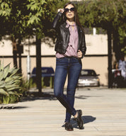 A woman in Maude jeans and an Oak Tree Farms leather jacket, exuding comfort with her wardrobe, stands confidently on a sidewalk.