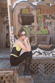 A woman, wearing Oak Tree Farms' Meryl vegetable tanned leather boots, sitting on a bench in front of a building covered in graffiti.