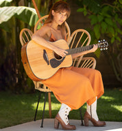 A woman in an orange dress playing an acoustic guitar while wearing an Oak Tree Farms Amelia leather welt boot.